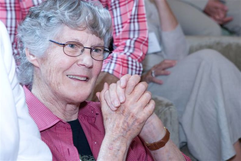 Ann Southam, clapping and smiling while sitting down