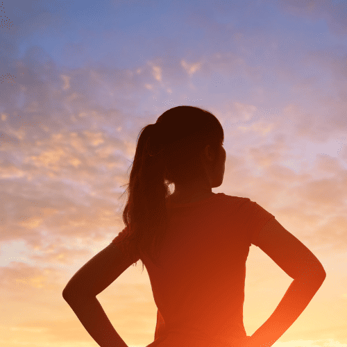 Image visual: silhouette of a girl with her hands on her hips facing the sunrise.